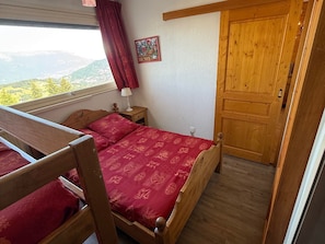 Quarto com cama de madeira, mesa de cabeceira, abajur, janela com vista e porta.