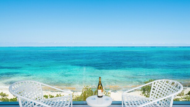 Ein Balkon mit zwei weißen Korbstühlen, der auf ein türkisblaues Meer unter blauem Himmel blickt.