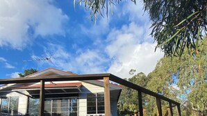 A modern house with a wooden deck, large windows, and a view of the surrounding greenery.