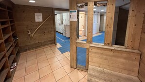 Un intérieur en bois avec un sol carrelé, une étagère en bois et une porte donnant sur une salle de bain où se trouve un tapis bleu.