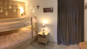 Un lit superposé décoré de guirlandes lumineuses, une table de chevet avec une lampe et un élément décoratif en forme de cœur accroché au mur.