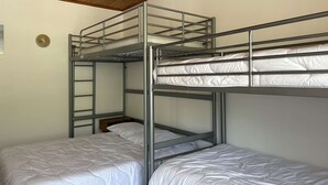 Een slaapkamer met een stapelbed, houten plafond en een wandlamp.