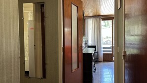 Een hal met houten deuren, een spiegel en uitzicht op een kamer met een raam en gordijnen.