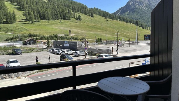 Een balkon met uitzicht op een parkeerplaats, een gebouw met de tekst 'GAREROUTIERIE' en een bergachtig landschap.