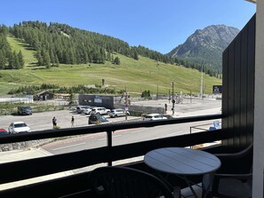 Ein Balkon mit Blick auf einen Parkplatz, ein Gebäude mit der Aufschrift 'GAREROUTIERIE' und eine gebirgige Landschaft.