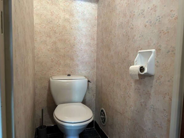A small bathroom with a toilet, a toilet paper holder, and a floor drain. - Comfort in the mountains, spacious studio 4 people, central Montgenèvre (Montgenèvre)