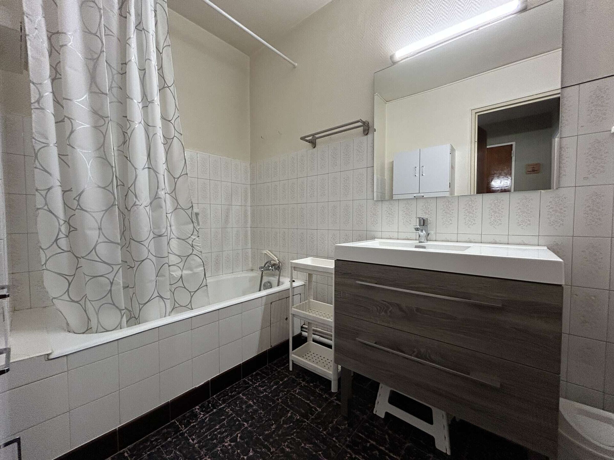 A modern bathroom with a bathtub, a vanity with a mirror, and a shower curtain with a leaf pattern.