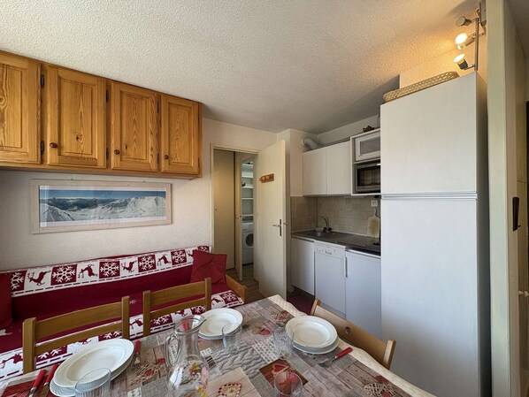 Une cuisine compacte avec des meubles en bois, une table à manger pour quatre personnes et un four à micro-ondes placé au-dessus du plan de travail.