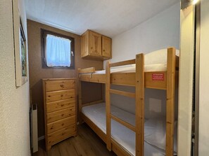 A compact room with bunk beds, a wooden dresser, a window with a curtain, and a wall-mounted cabinet.