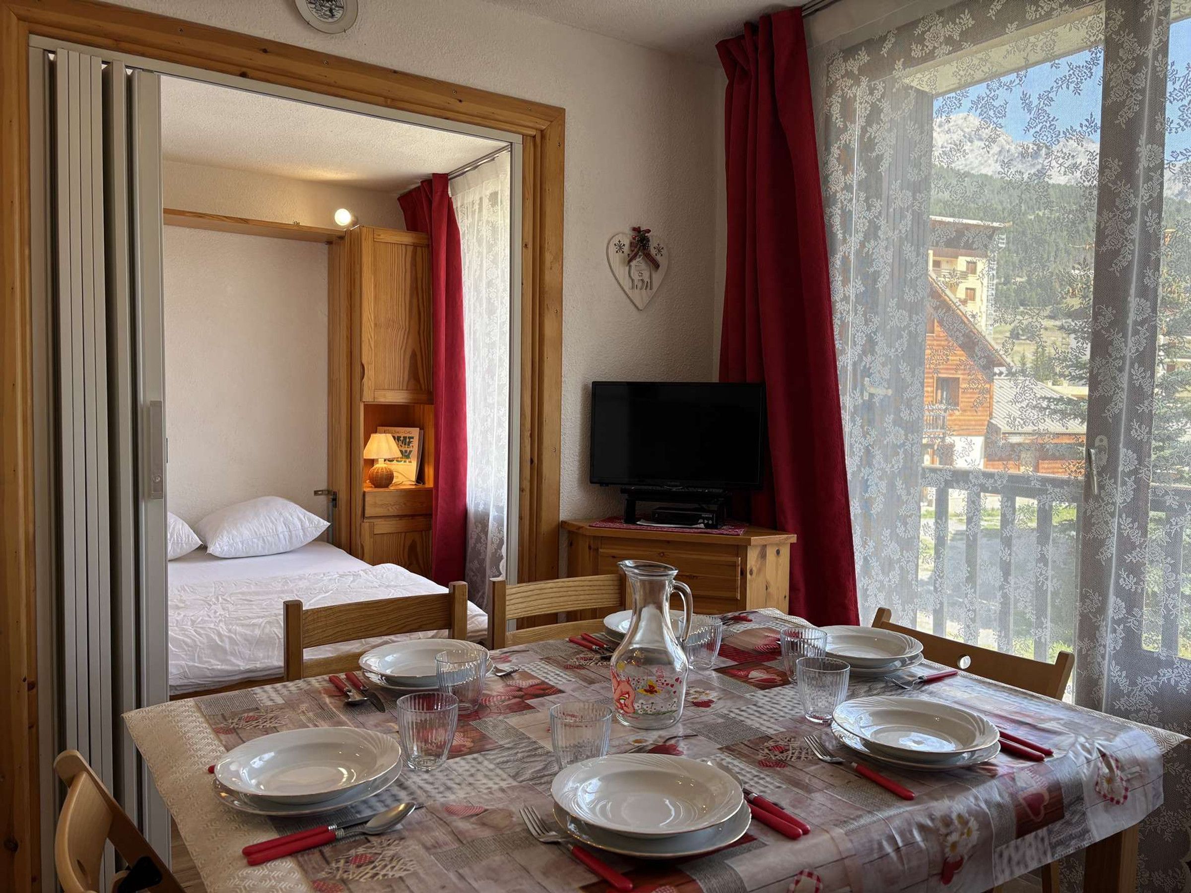 A room with a bed, a television, and a dining table set for four.