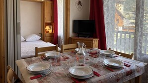 A room with a bed, a television, and a dining table set for four.