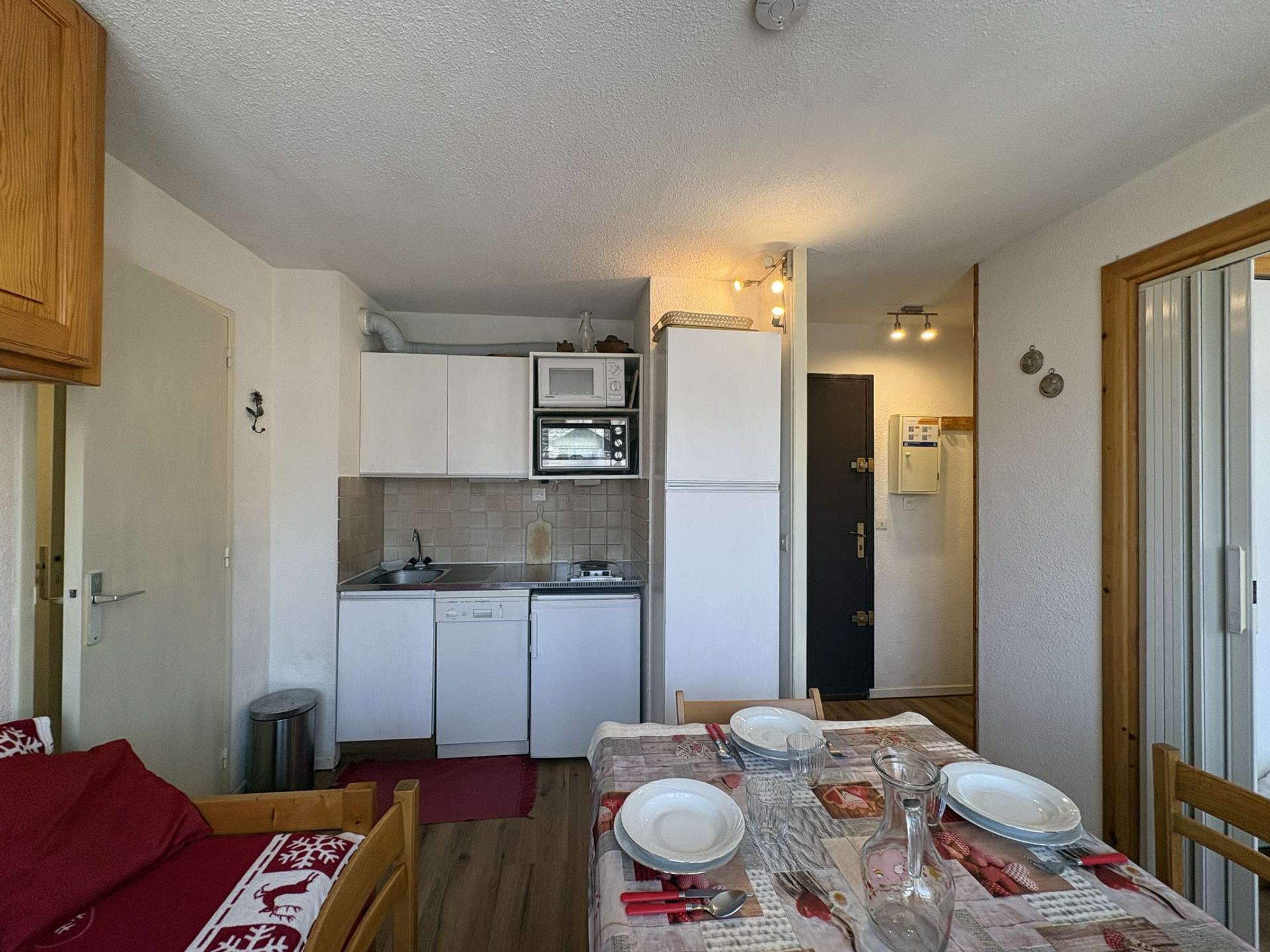 Eine kleine Küche mit Mikrowelle, Toaster und Kühlschrank, ein Esstisch mit Tellern und Besteck sowie eine kleine Mülltonne.