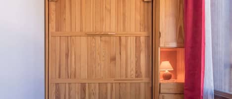A wooden wardrobe with a sliding door, a red curtain, and a lamp in a wooden cabinet.