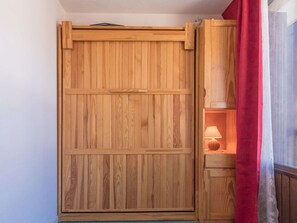 A wooden wardrobe with a sliding door, a red curtain, and a lamp in a wooden cabinet.