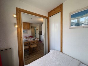 A bedroom with a bed, a wooden door, and a view of a dining area with a table and chairs. - Apartment Montgenèvre - 2 bedrooms, balcony, washing machine, TV (Montgenèvre)