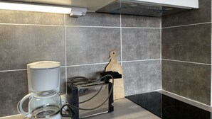 A modern kitchen with grey tiles, a coffee maker, a toaster, and a hanging wooden cutting board. - Cozy Ski Studio for 2 in Montgenèvre with Parking and Balcony (Montgenèvre)