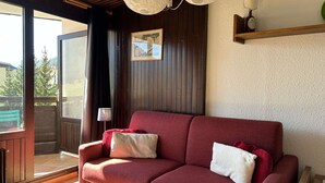 A red sofa with white cushions in a room with wooden paneling, a framed picture on the wall, and a lamp on a shelf. - Cozy Ski Studio for 2 in Montgenèvre with Parking and Balcony (Montgenèvre)