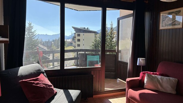 A room with a large window, a red sofa, a grey sofa, and a lamp. - Cozy Ski Studio for 2 in Montgenèvre with Parking and Balcony (Montgenèvre)