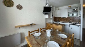 Une cuisine compacte avec un coin repas, un téléviseur fixé au-dessus du comptoir et un petit réfrigérateur.