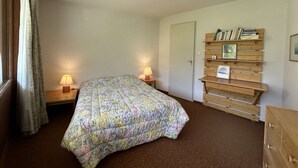 Un dormitorio con cama, dos lámparas de noche, una estantería de madera y una puerta.