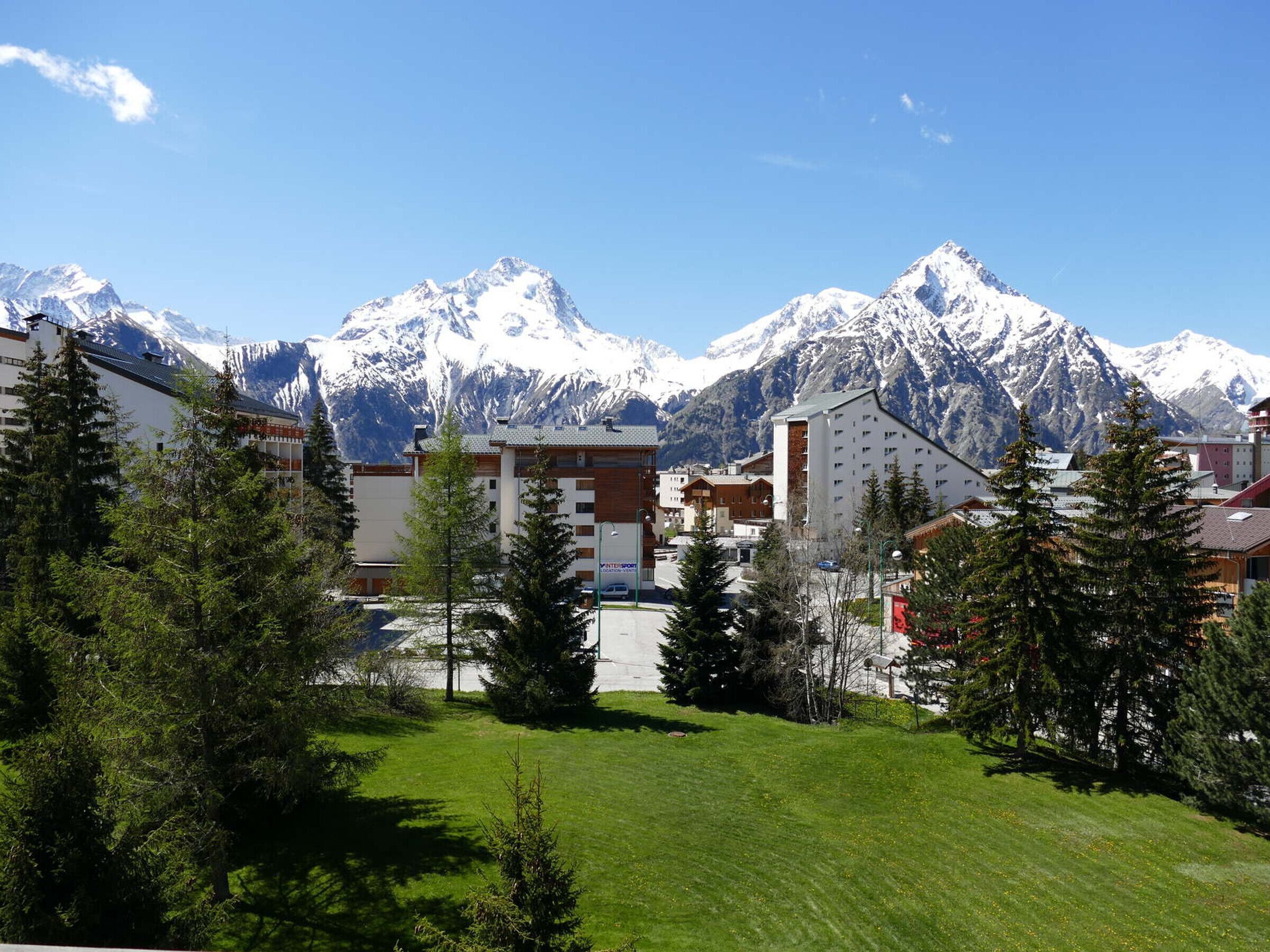 Un hôtel offrant une vue sur des montagnes enneigées, entouré de verdure et de bâtiments modernes.
