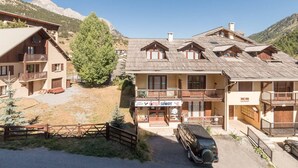 Un chalet de montagne doté de plusieurs balcons, un magasin de location de matériel de ski et un VUS garé.
