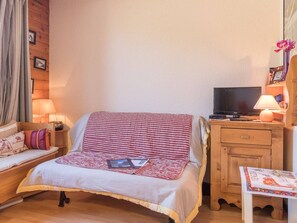 Quarto aconchegante com cama, televisão, mesa de cabeceira com abajur e uma pequena mesa com um objeto decorativo.