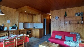 A cozy wooden interior with a dining area, kitchen, and a red sofa.