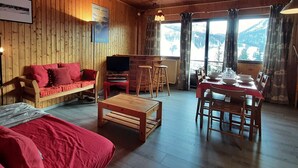 A cozy wooden cabin interior with a sofa, TV, dining table, and chairs.