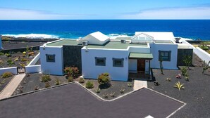Ein Küstenhaus mit flachem Dach, vielen Fenstern und einer kleinen Veranda.