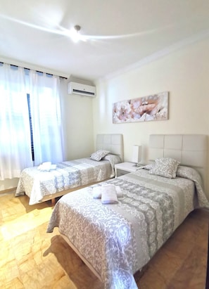 Una camera d'albergo con due letti, una ventola a soffitto, un condizionatore d'aria e un quadro appeso al muro.