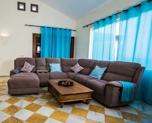 A living room with a brown sectional sofa, a wooden coffee table, and blue curtains.