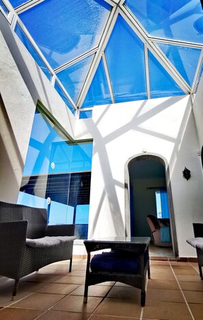 A sunlit interior with a geometric glass ceiling, wicker furniture, and a tiled floor.