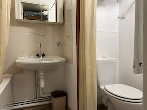 Kylpyhuoneessa on valkoinen pesuallas, wc ja suihku. Pesualtaan yläpuolella on kaappi ja osa verhosta on näkyvissä.
