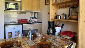 Een compacte keuken met houten kastjes, een magnetron, een koffiezetapparaat en een eettafel met glazen en borden.