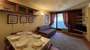 A dining area with a table set for four, a sofa, and a TV. - Ski-in/Ski-out 6 Pax Apartment, Montgenèvre with East Balconies and Modern Amenities (Montgenèvre)