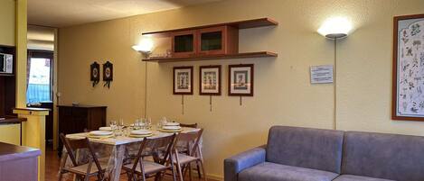 A dining area with a table set for four, a grey sofa, and framed botanical prints on the wall.
