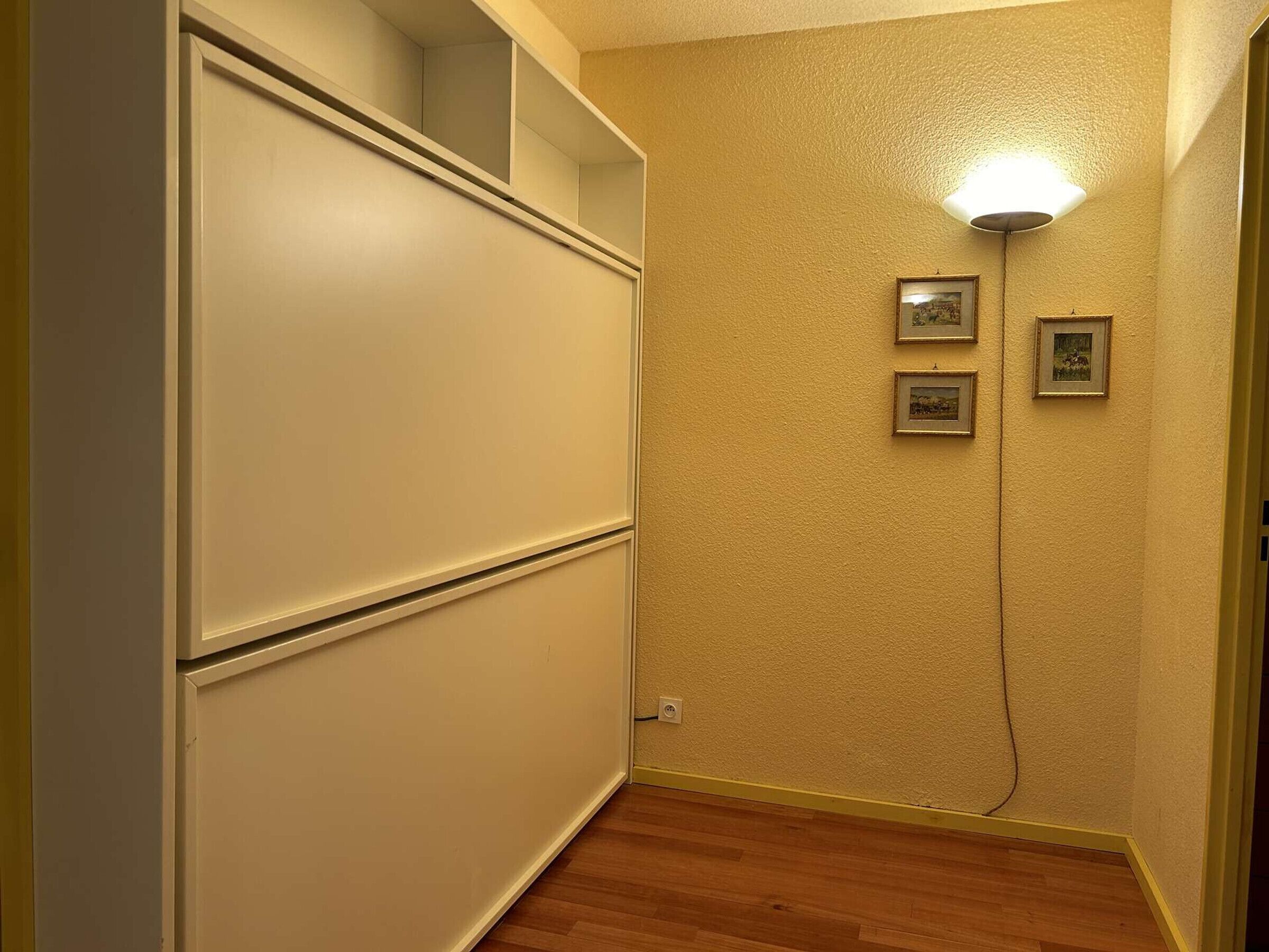A hallway with a wooden floor, a white cabinet, and a wall-mounted light fixture.