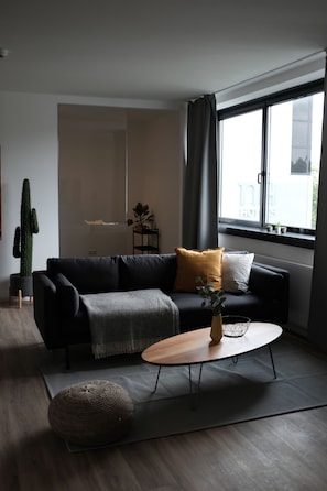 Ein modernes Wohnzimmer mit einem dunklen Sofa, einem Holztisch und einer Topfpflanze.