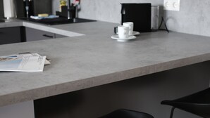 A modern kitchen with a grey countertop, black bar stools, and a coffee machine. - aparthotel glück auf Düppelstrasse (Oberhausen)