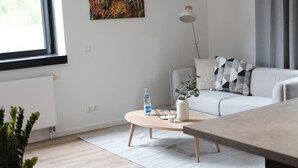 A modern living room with a sofa, a coffee table, a plant, and a painting on the wall. - aparthotel glück auf Düppelstrasse (Oberhausen)