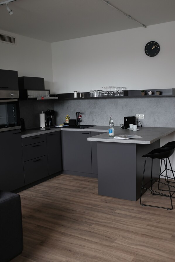 A modern kitchen with dark cabinetry, a central island, and a clock on the wall.