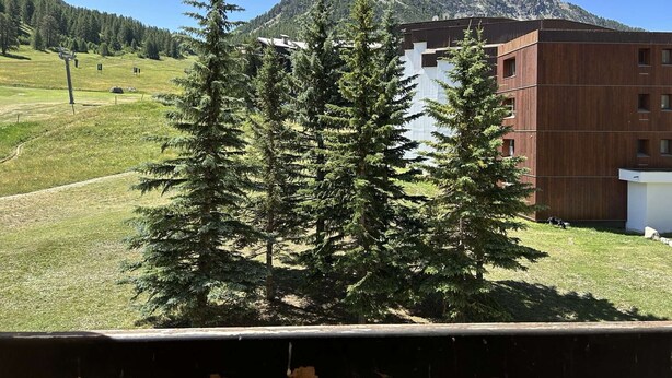 A building with a modern design, surrounded by a grassy area and trees, with a mountain in the background. - Modern studio PMR, south balcony sleeps 4 - Montgenèvre (Montgenèvre)