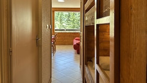A wooden interior with a tiled floor, a window with a view of greenery, and a red chair. - Modern studio PMR, south balcony sleeps 4 - Montgenèvre (Montgenèvre)