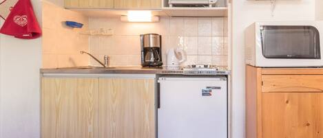 Eine kleine Küche mit Holzschränken, einer eingebauten Mikrowelle, einer Kaffeemaschine und einem kleinen Kühlschrank.