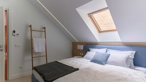 Camera da letto con lucernario, una scala in legno, un letto con biancheria da letto bianco e blu e un pannello di controllo a parete.