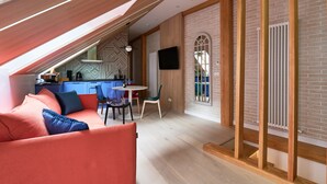 Camera da loft moderna con soffitto spiovente, travi in legno a vista, angolo cottura integrato, zona pranzo e televisore a parete.