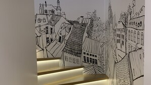 Una scala con gradini in legno e bordi illuminati, che conduce a un muro con un murale di un paesaggio urbano in bianco e nero.