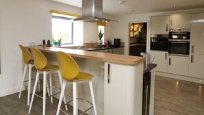 Une cuisine moderne dotée d’un îlot central, de tabourets de bar, d’appareils électroménagers en acier inoxydable et d’une grande fenêtre.