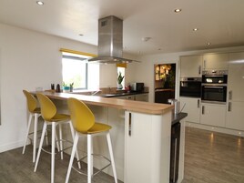 A modern kitchen with a central island, bar stools, stainless steel appliances, and a large window.